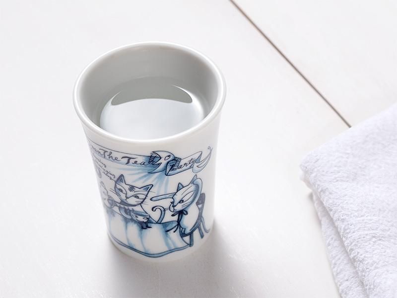 清潔な白いテーブルの上に置かれたタンブラーのアップ画像。タンブラーには、青い線で描かれた猫たちのイラストがはっきりと見える。透明な水が口元近くまで注がれており、右横には白いタオルが畳んで置かれている。丁寧に暮らすアイテムとして、ティータイムのお供に最適なタンブラー。