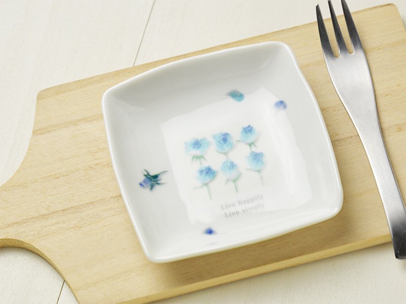 美濃焼製の白い小皿に雑貨デザイナーシンジカトウさんが珍しいブルーのバラのイラストを描いた小皿の画像です。