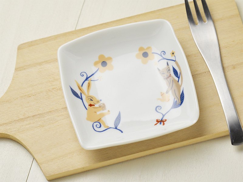 美濃焼製の白い小皿に雑貨デザイナーシンジカトウさんが猫とうさぎのイラストを描いた小皿の画像です。