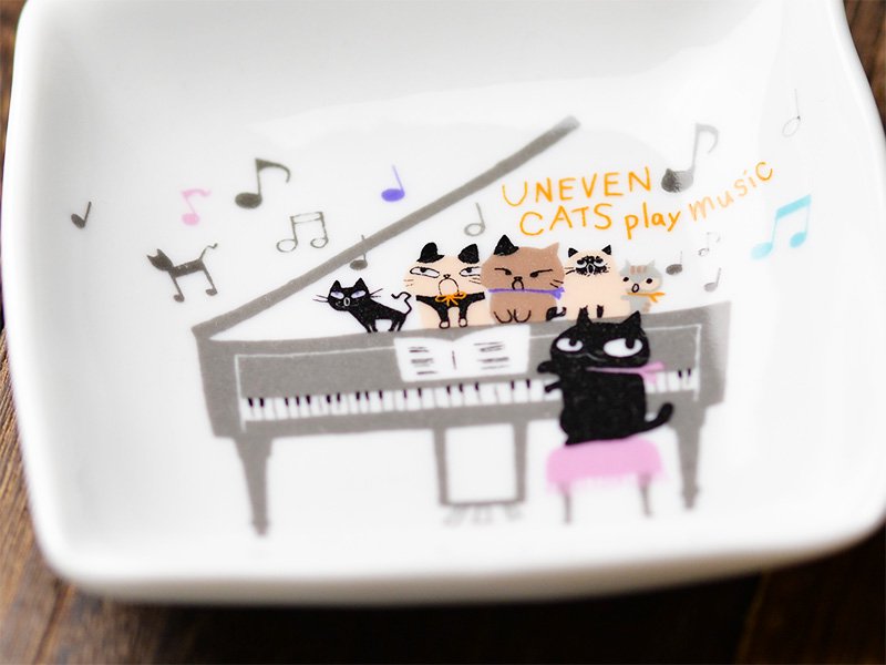 美濃焼製の白い小皿に雑貨デザイナーシンジカトウさんが黒猫がピアノを弾き5匹の猫が鍵盤の上で合唱するユーモラスなイラストを描いた小皿のをデザインが分かるようにデザイン部分を大きく拡大した画像です。